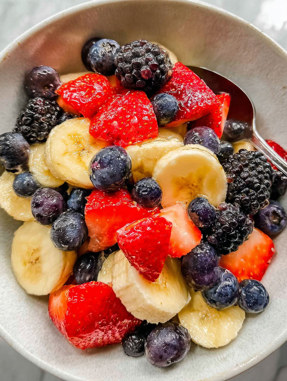 A bowl of fruit salad with bananas, strawberries, blueberries, and blackberries.