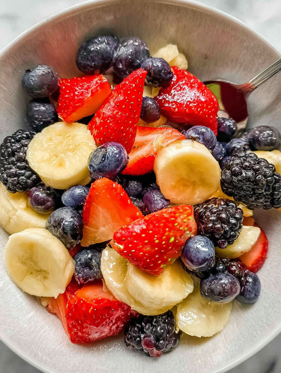 A bowl of fruit salad with bananas, strawberries, blueberries, and blackberries.