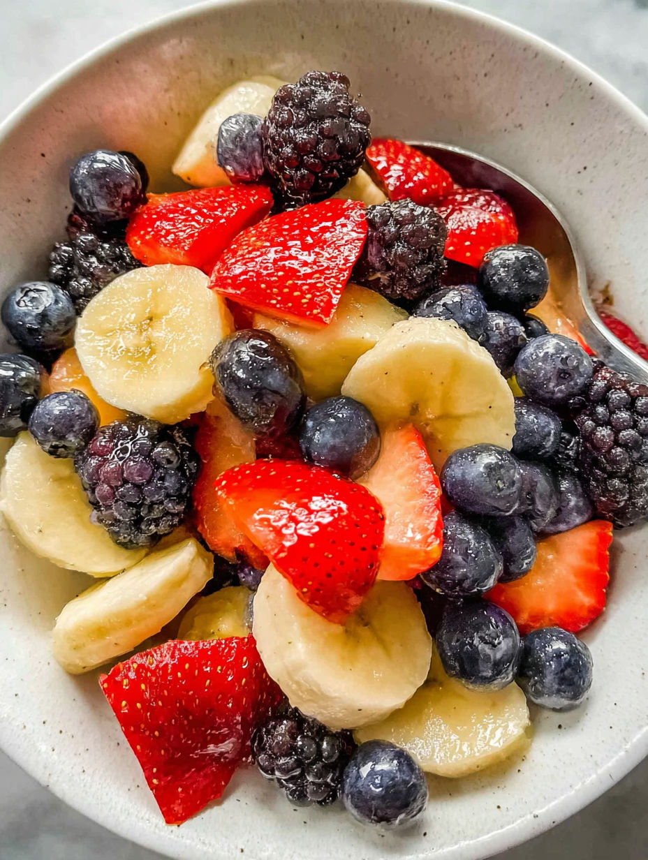 A bowl of fruit salad with bananas, strawberries, blueberries, and raspberries.