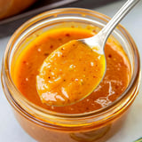 Jar of orange mustard sauce with a spoon inside.