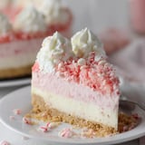 A creamy cake slice topped with white icing and red cookie crumbles.