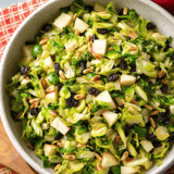 A bowl full of greens, apples, and nuts sitting on a table.