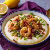 A bowl of shrimp and grits with a lemon wedge on the side.