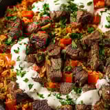 Chunks of steak on rice covered with white cheese sauce.