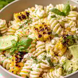A bowl packed with pasta, cheesy corn, and fresh toppings.