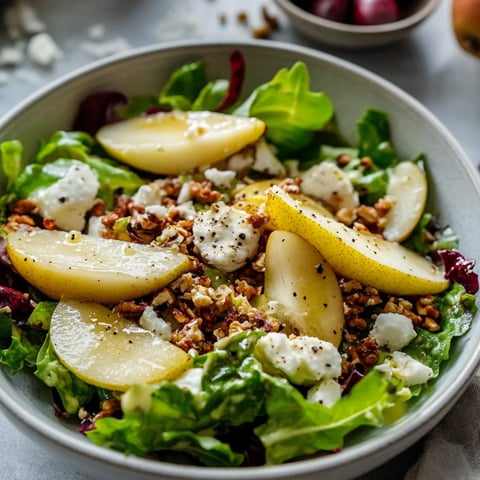 Bowl of tossing salad with feta crumbles and pear slices.