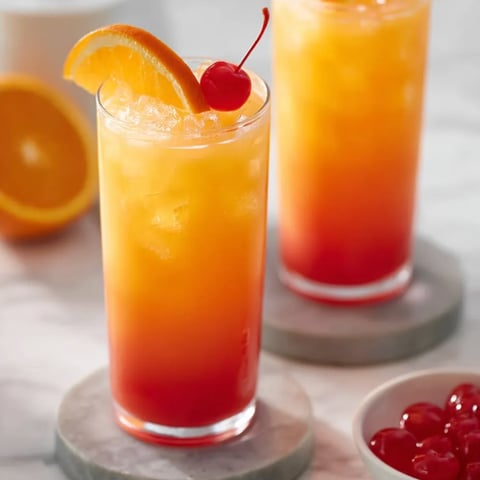 Two tall glasses packed with orange drink and cherries nearby.