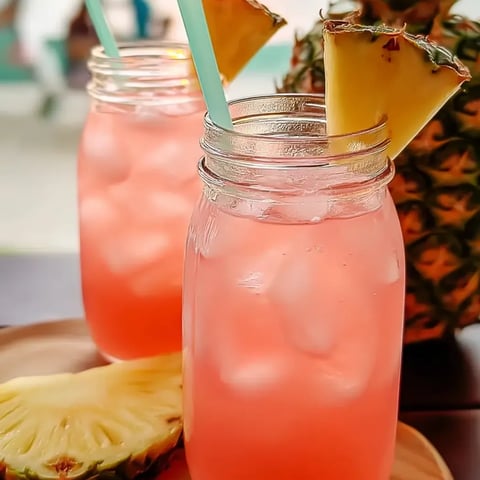 Pink drinks in two glasses with pineapple slices inside.