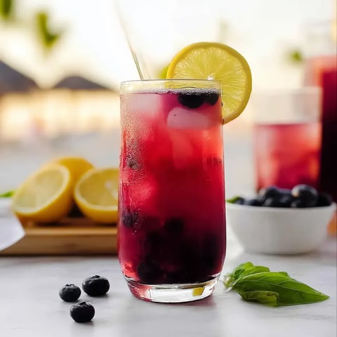 A glass of red juice with lemon and blueberries.