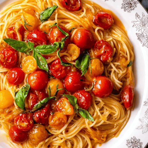 Bowl of pasta with tomatoes and basil leaves on top.