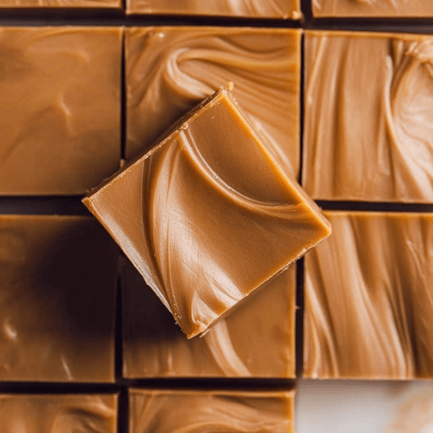 Square piece of caramel coffee fudge sits on a plate, showing caramel ripples.