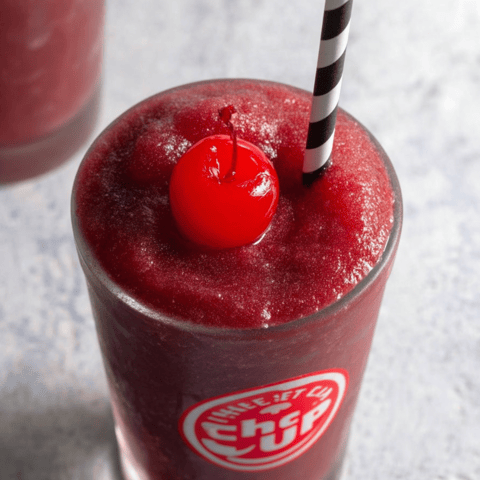 A chilled glass filled with red slushy and a cherry sitting on top.