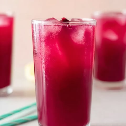 Glass filled with red fruit drink and ice cubes.