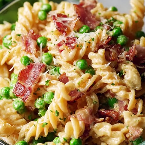 A bowl packed with pasta, green peas, and bites of bacon.