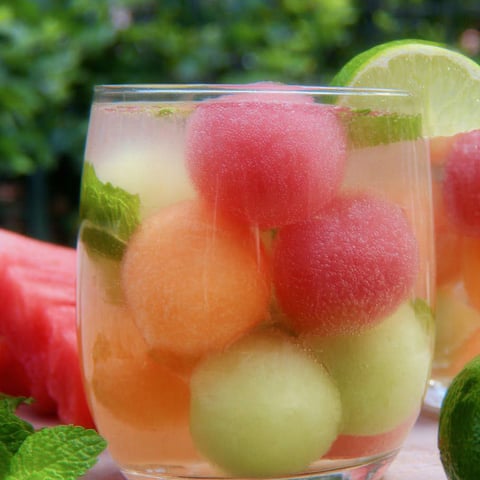 Watermelon juice in a glass with lime and fresh melon on the rim.