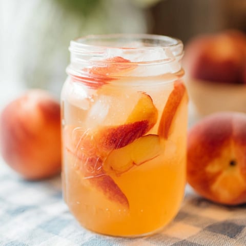 Glass full of peach lemonade with a peach chunk inside.