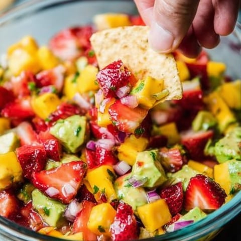A hand is picking up a chip from a bowl filled with colorful fruit mixture.